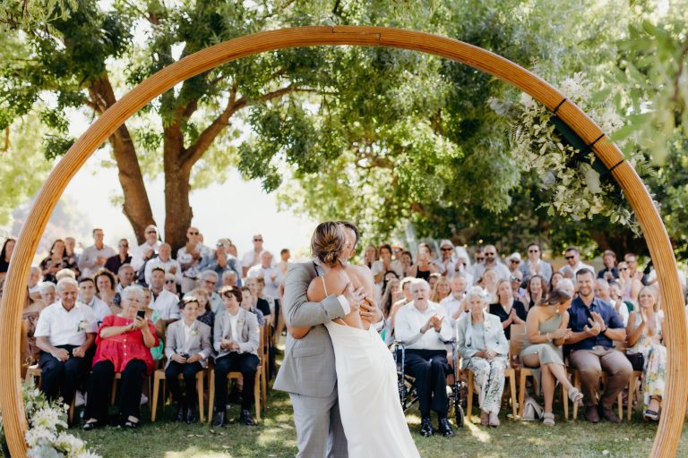 Bride and groom first kiss, guests celebrating in the background