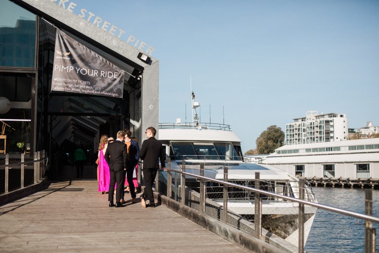 Guests dressed in formal wear waiting at a pier in front of a white catamaran
