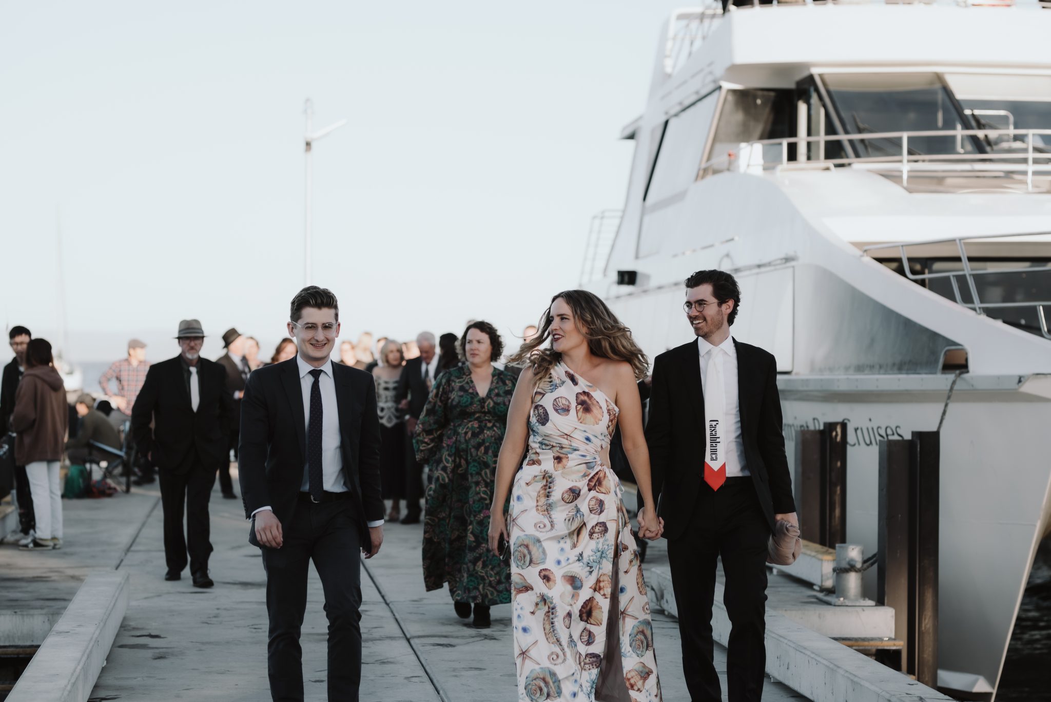 Wedding guests dressed in formal wear walking along a jetty