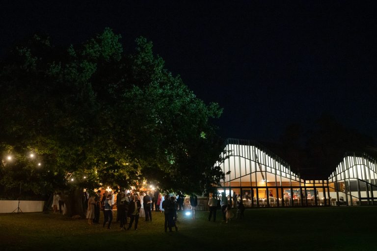 Peppermint Bay function space lit up at night time with guests mingling on the lawn